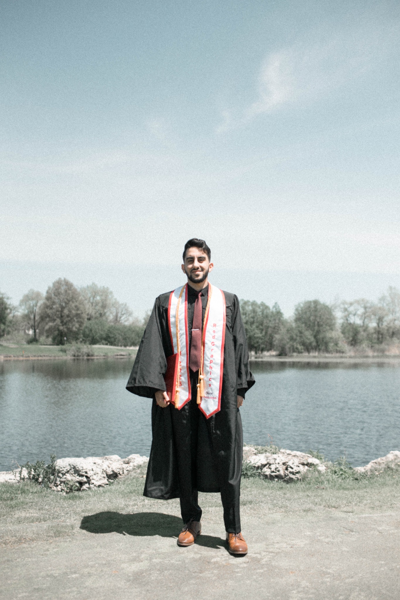 Noor Rachid in graduation regalia beside a lake